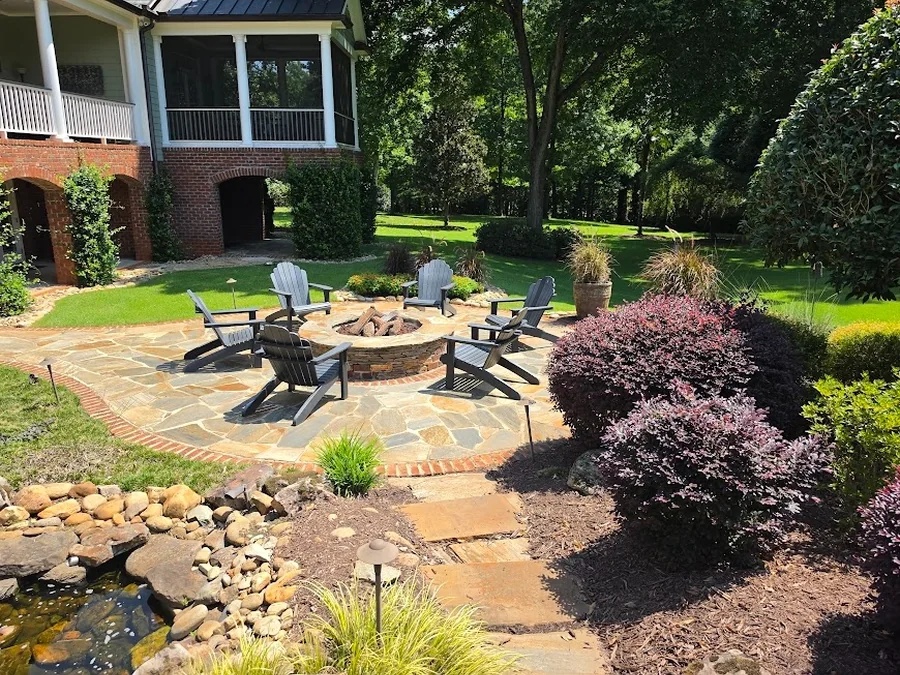 A flagstone-and-brick fire pit patio set right beside a koi pond and waterfall, with layered plantings tying it into the lawn. A full backyard built for evenings outside, in the Upstate.