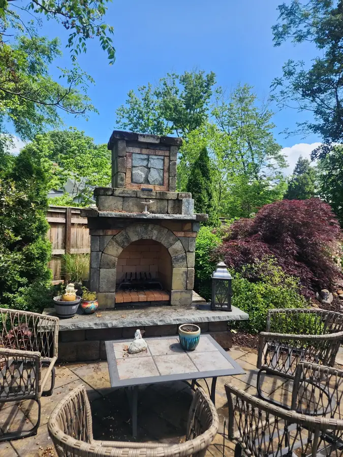 An arched stone fireplace framed by mature plantings to make an outdoor room — a quiet retreat for a Greer artist to enjoy the evenings.