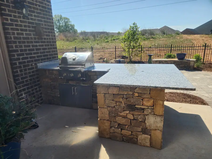 Stacked stone base, granite top, built-in grill — built to sit outside in Carolina weather for decades. The centerpiece for entertaining in this Greer courtyard home.
