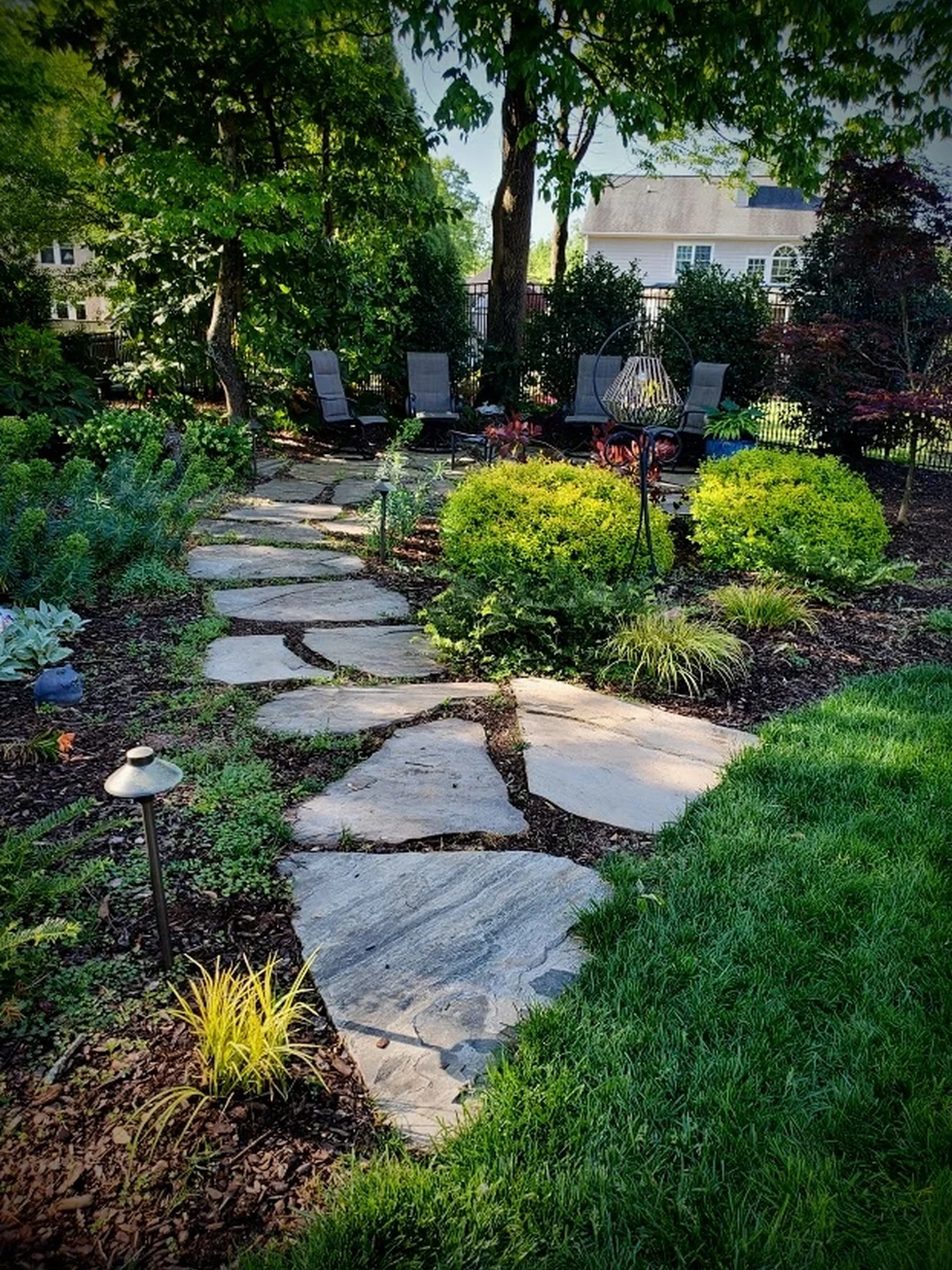 Natural stepping-stone flagstone leading from the lawn into a fire pit seating area, framed with boxwood and ornamental grasses. Part of a full backyard build in the Upstate.