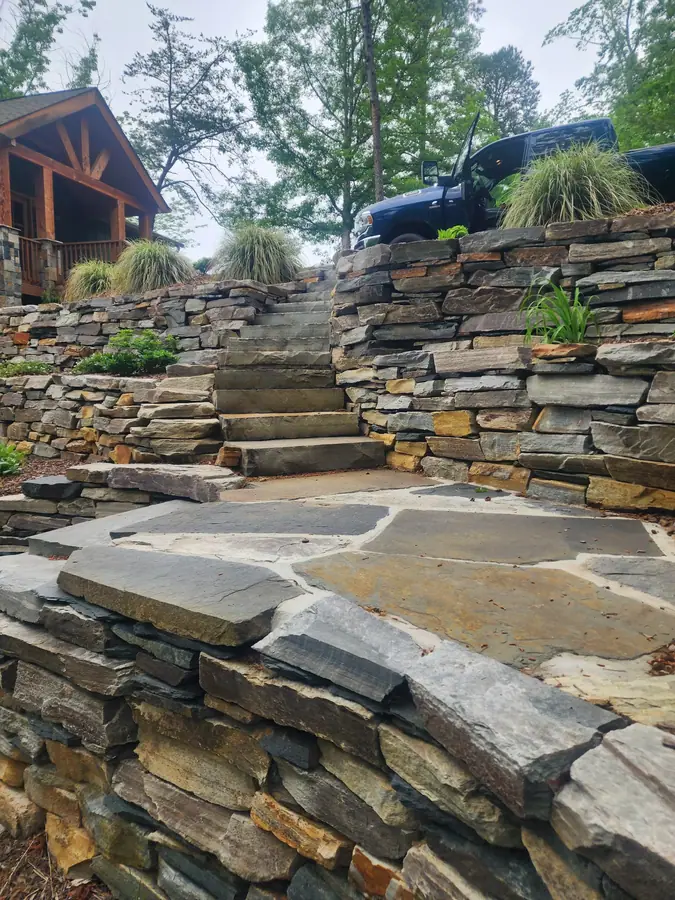 Hand-stacked wall blending slate and flagstone in earth tones — no two courses the same. This Lake Lure restoration saved the hillside from collapsing after Hurricane Helene.