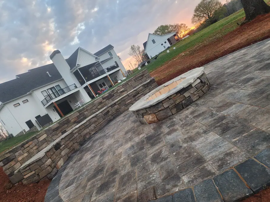 Paver patio anchored by a stone retaining wall that doubles as a bench, with a built-in fire pit. Built on Silver Lake in Duncan for cozy late-summer nights.