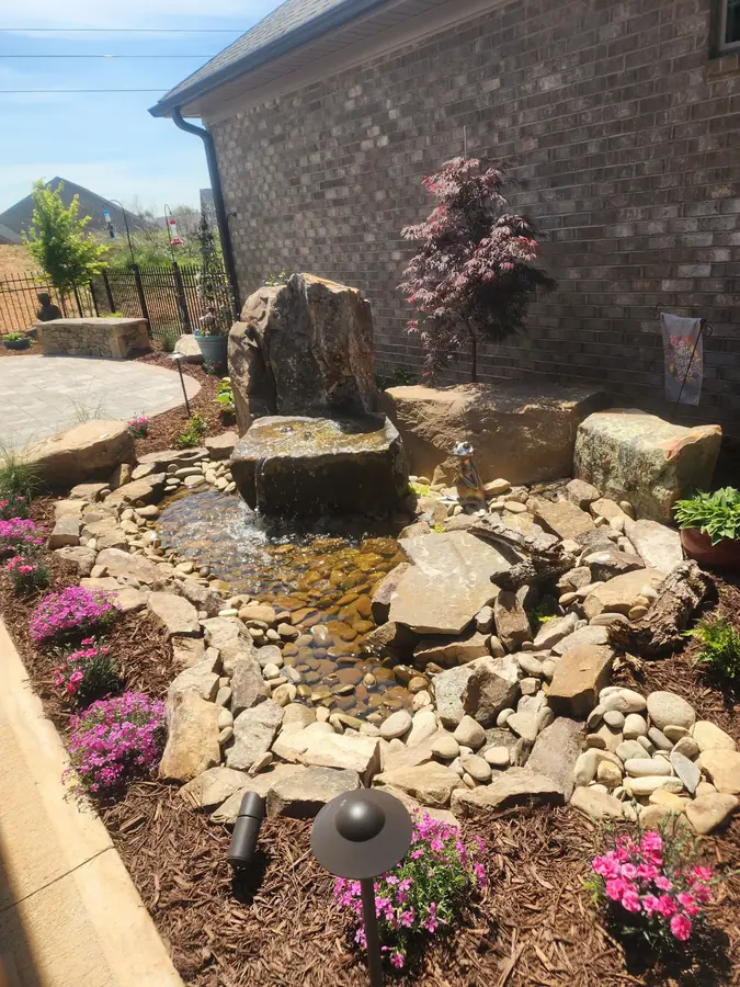 Feature boulder set into a planting bed with seasonal color around the base — a courtyard centerpiece in Greer.