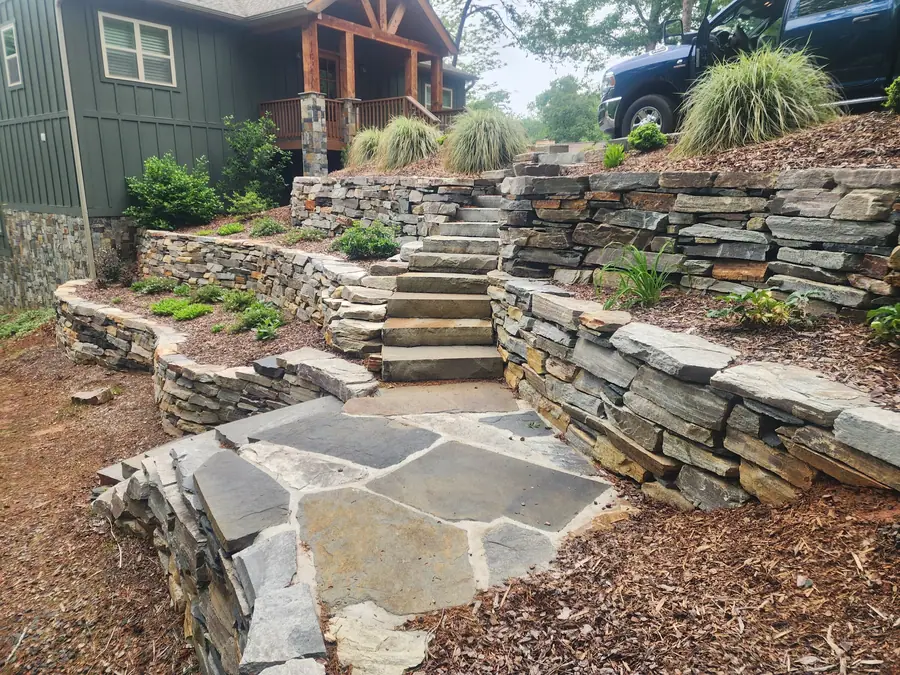 Two terraced walls with stone treads and a flagstone landing, turning an unusable bank into garden space. This Lake Lure hillside was at risk of collapsing and taking the driveway with it after Hurricane Helene — now it's an inviting garden with a view of Chimney Rock.