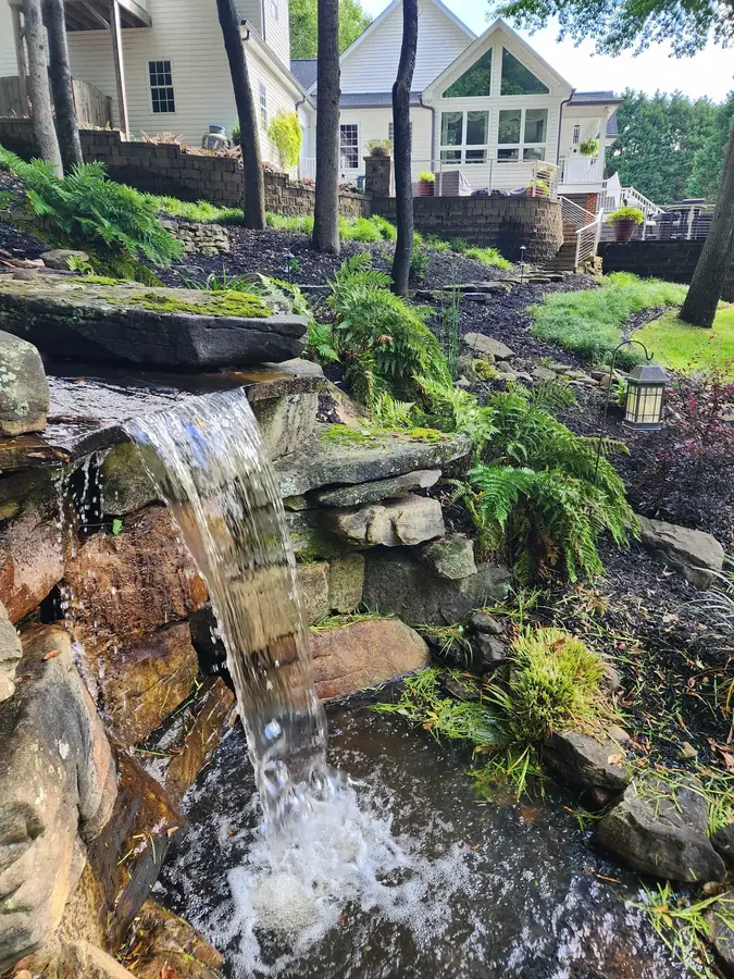 A natural creek rebuilt with moss-set boulders and log edging so it runs clean and looks like it was always there. What was a muddy hole in Simpsonville is now a backyard oasis.
